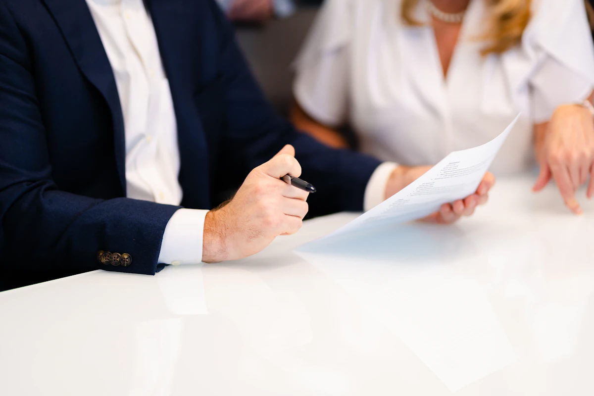 Two people in business dress passing a document across a table